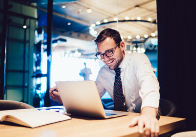 Happy Businessman Sitting At Office Desk Looking At Computer Screen